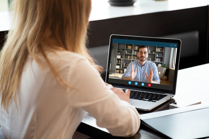 A woman uses her laptop to speak with a man on a video call to represent insurance sales associate coaching.